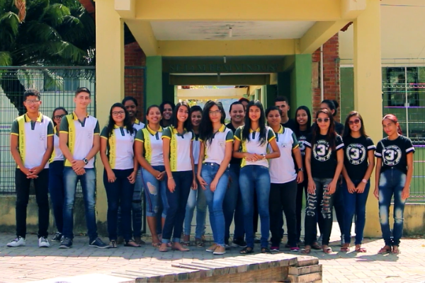 Um grupo de trinta alunos, em uniforme escolar, posam na frente de uma escola.