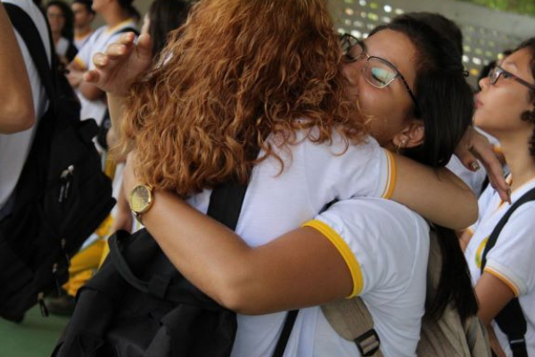 Duas meninas estão se abraçando vestidas com camisetas de uniforme de escola
